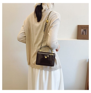 Glossy black patent leather mini crossbody bag with gold metal handle on a model