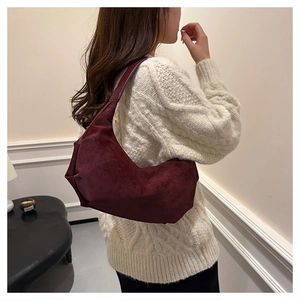 Close-up of a burgundy suede hobo bag carried by a model in a cozy indoor setting