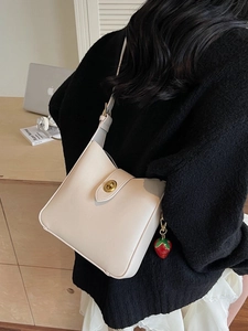 Chic cream leather bucket bag with gold clasp and strawberry charm on a female model