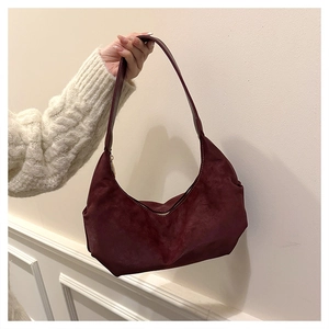 Detailed view of burgundy suede hobo bag held by hand against a minimalist wall