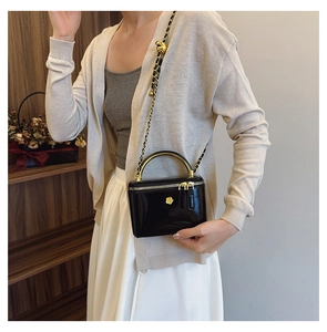 Detail of black glossy leather crossbody bag with gold metal handle and chain strap