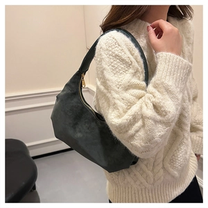 Detail of dark green suede hobo bag with gold zipper held by a model in a beige sweater