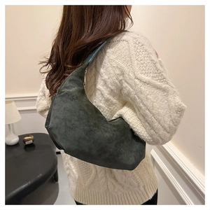 Close-up of a dark green suede hobo bag with a gold zipper on a knit sweater
