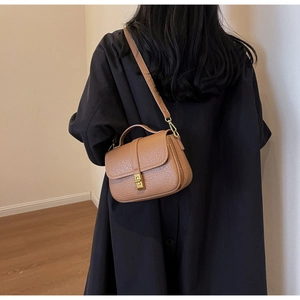 Close-up of brown pebbled leather texture and golden metal twist lock on shoulder bag