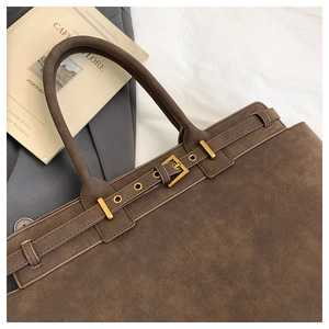 Detail of brown suede tote bag featuring parallel straps and gold square metal buckles