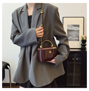 Close-up of a glossy burgundy crossbody bag with golden metal handle and flower clasp