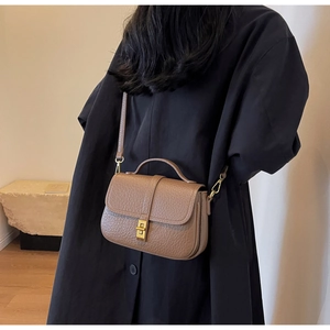 Detailed shot of brown litchi pattern leather bag with gold buckle on stone base