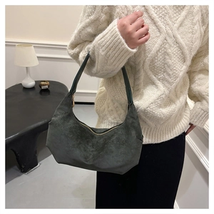 Dark green suede dumpling bag with gold zipper shown on model in white sweater