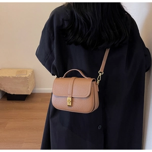 Detail of camel brown leather crossbody bag featuring gold twist lock and pebble texture