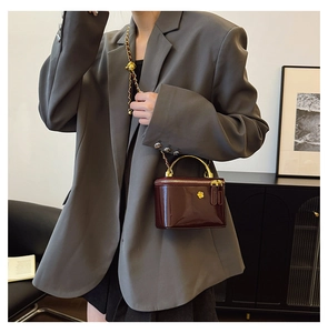 Detail of burgundy patent leather handbag with gold flower clasp worn with grey blazer