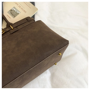 Detailed close-up of dark brown suede tote bag with golden buckles and metal feet