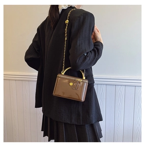 Brown patent leather mini square bag with gold handle and flower logo on model