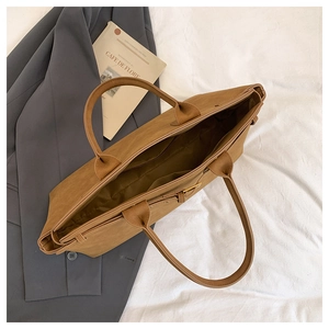 Detail of spacious camel brown tote bag with slim handles and side metal buckle design