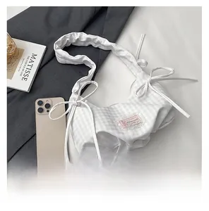 Detail of grey plaid pleated shoulder bag featuring a decorative bow and pink brand label