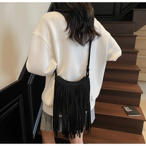 Detail of black suede fringe crossbody bag with long tassels shown on a model