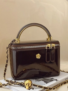 Brown patent leather vanity bag with golden chain strap and top handle on a magazine