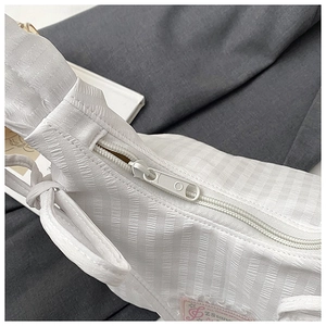 Close-up of white textured plaid fabric with zipper and pink brand tag on the shoulder bag