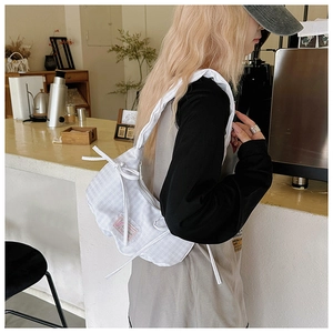 Close-up of white pleated shoulder bag featuring a decorative bow on the strap