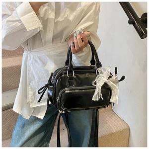 Detail der schwarzen Lackleder-Boston-Bag mit weißer Organza-Schleife und Perlenkette