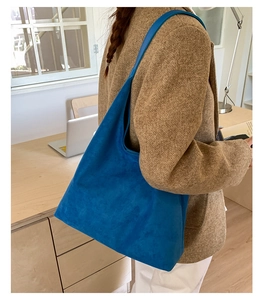 Detalle de bolso tote de ante azul Klein con correa ancha de hombro sobre blazer marrón