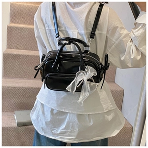 Detail eines schwarzen Mini-Rucksacks mit weißer Spitzenschleife und Perlen-Metallkette