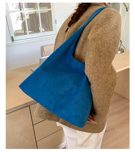 Vista detallada del bolso tote grande azul Klein en ante mate con chaqueta camel