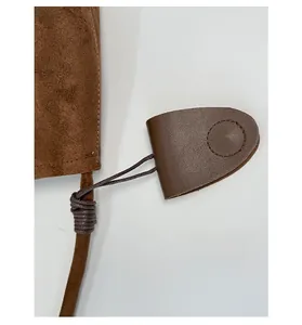 Detail of a brown suede shoulder bag featuring a matching leather charm and fine stitching