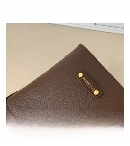 Dettaglio pelle martellata marrone scuro con rivetti dorati e logo del marchio sul secchiello