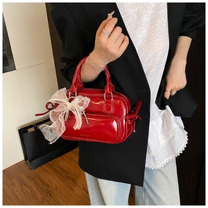 Detail einer roten glänzenden Handtasche mit großer weißer Spitzen-Schleife und Glanz