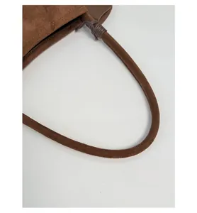 Detail of a brown suede shoulder bag showing cylindrical handle with cord wrap decoration