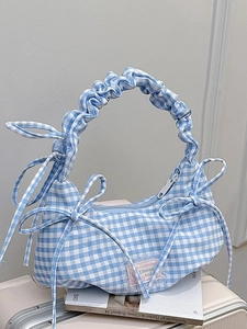 Blue plaid ruffled shoulder bag with ribbon bow accents on a white suitcase background