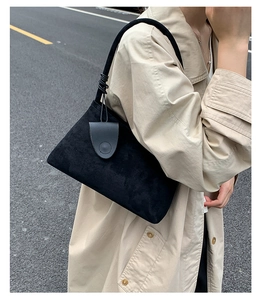 Detail of black suede underarm bag with unique knot shoulder strap on trench coat