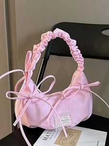 Pink striped baguette bag with bow details and ruffled handle on an artistic backdrop