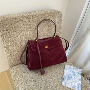 Détail du sac à main en daim bordeaux avec fermoir doré posé sur une chaise élégante