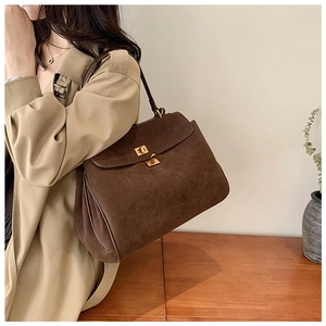 Sac fourre-tout mat marron foncé avec fermoir doré porté par un mannequin en trench
