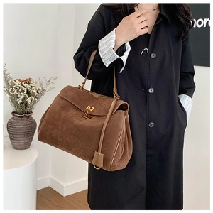 Détail d'un grand sac à main en daim marron avec un fermoir rotatif en métal doré sur le rabat