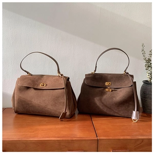 Vue détaillée des sacs à main en daim mat avec fermoirs dorés et poignée sur socle en bois