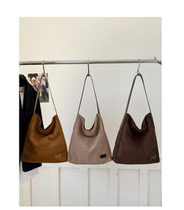 Trois sacs cabas en daim en couleurs caramel, beige et café foncé suspendus sur un portant