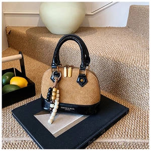 Detail of quilted brown suede shell bag featuring beaded tassel on a black book