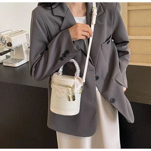 Detail of white woven cylinder bucket bag with scarf-wrapped handle and gold lock hardware