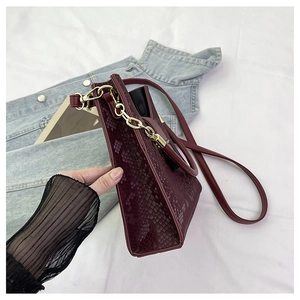 Détail du sac bordeaux à motif serpent avec chaîne dorée et structure de texture latérale