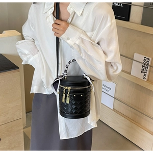 Detail of a black quilted cylinder bucket bag with a silk scarf handle and gold hardware