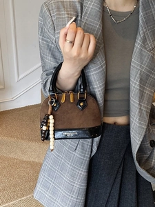 Brown and black shell-shaped handbag with quilted stitching and bead charm on a model