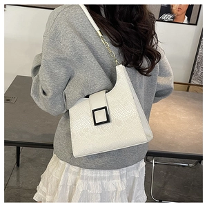 Détail du sac blanc à motif crocodile avec boucle noire et bandoulière en chaîne dorée