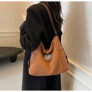 Detail einer großen braunen Leder-Beuteltasche mit silbernem M-Logo über der Schulter
