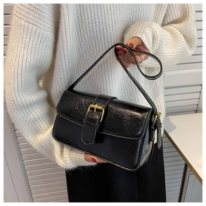 Detailed close-up of a black patent leather shoulder bag featuring a vintage gold buckle