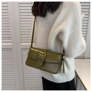 Detail of dark green vintage shoulder bag with metal buckle on white sweater