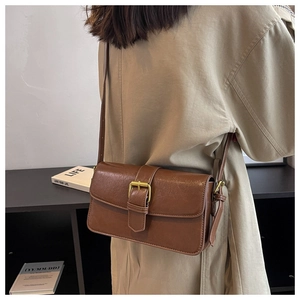 Close-up of a vintage brown leather crossbody bag with a gold buckle on a beige coat
