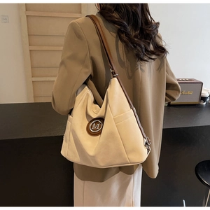 Detail einer beigen Canvas-Tasche mit Seitentasche und braunem Leder-M-Logo-Patch
