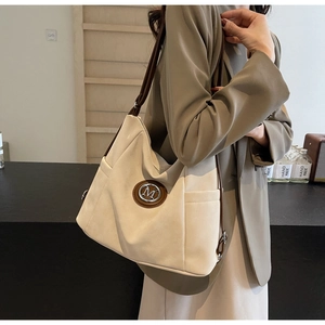 Detailaufnahme der beige Tragetasche mit braunen Trägern und rundem M-Metalllogo